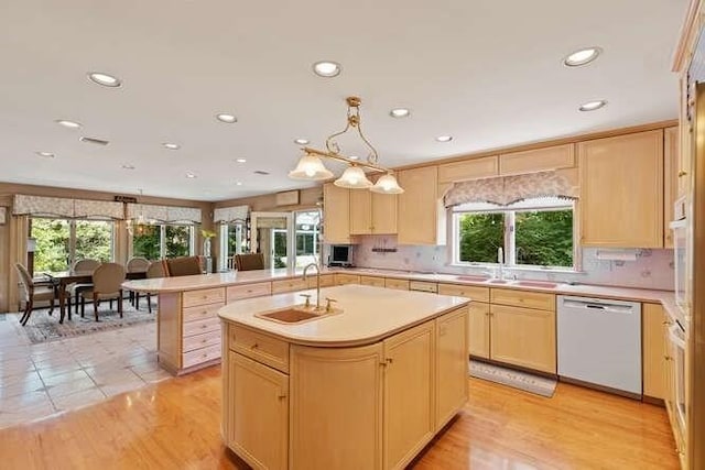 kitchen featuring white appliances, light countertops, a sink, and light brown cabinetry