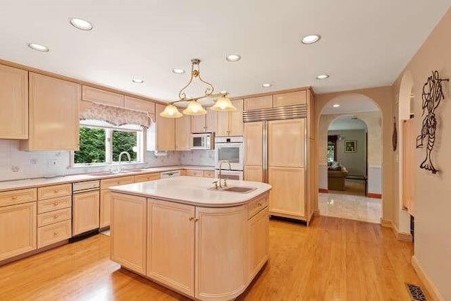 kitchen featuring white microwave, arched walkways, light countertops, paneled built in fridge, and light brown cabinets