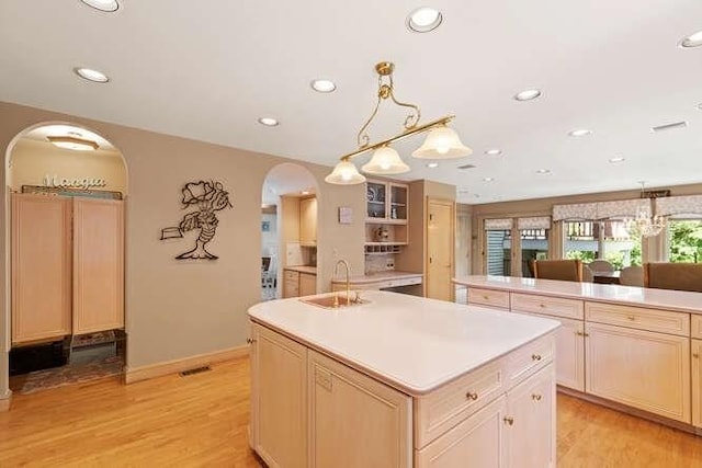 kitchen featuring light wood-type flooring, light countertops, a center island with sink, arched walkways, and a sink