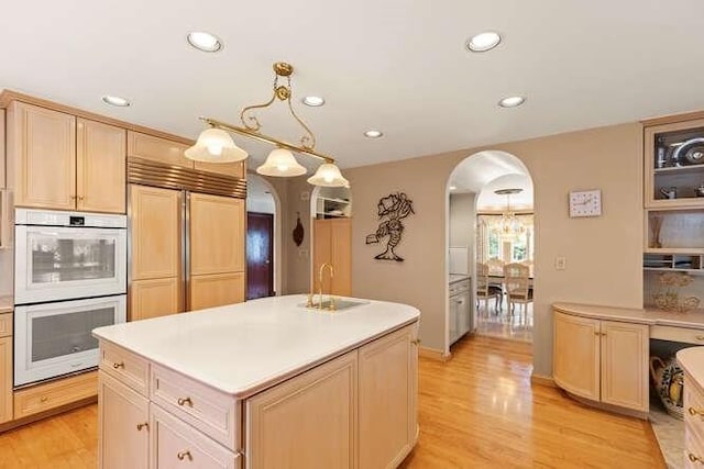 kitchen featuring double oven, light wood-style flooring, arched walkways, a sink, and paneled built in fridge
