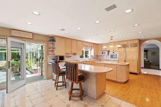 kitchen featuring stainless steel microwave, light brown cabinets, light countertops, a kitchen island, and arched walkways