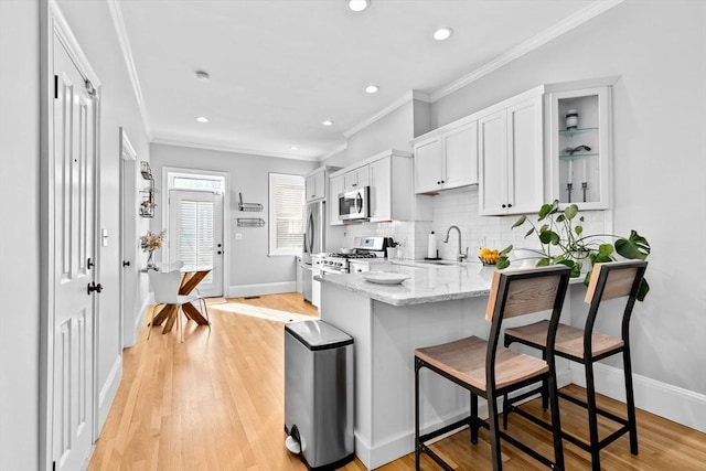 kitchen featuring tasteful backsplash, a peninsula, light stone countertops, stainless steel appliances, and crown molding