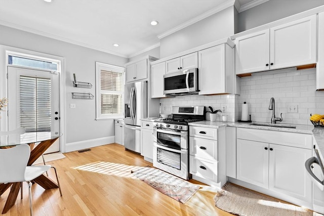 kitchen with a sink, white cabinets, ornamental molding, appliances with stainless steel finishes, and light wood-type flooring