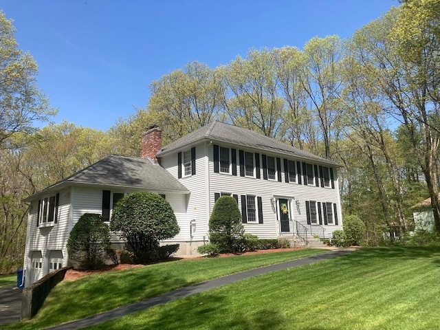 colonial home with a chimney, a front lawn, and roof with shingles