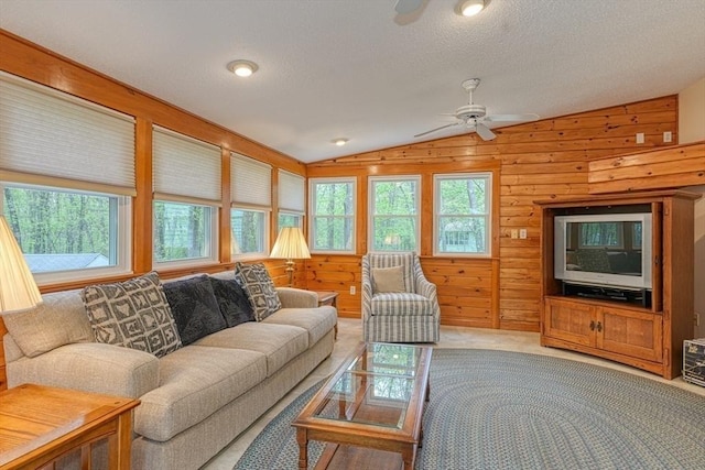 living area featuring vaulted ceiling, ceiling fan, wood walls, light colored carpet, and a textured ceiling