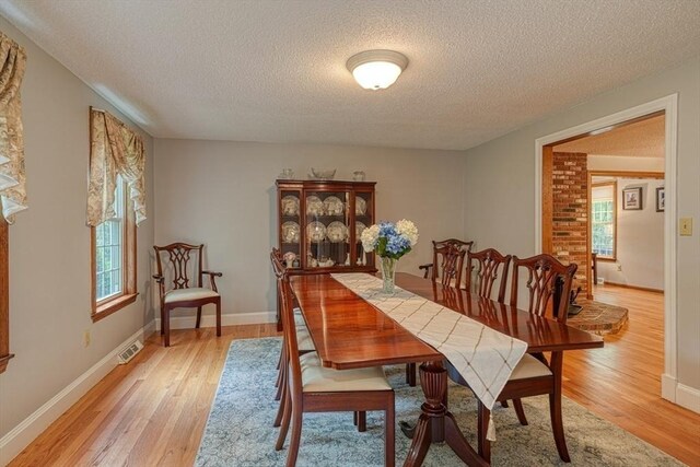 dining space featuring a textured ceiling, light wood finished floors, and baseboards