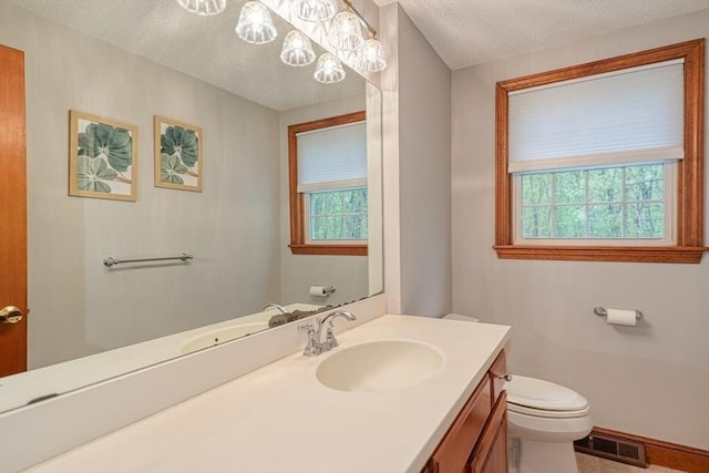 half bath with toilet, healthy amount of natural light, a textured ceiling, vanity, and a chandelier