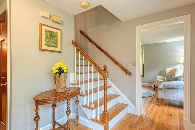 staircase with wood finished floors, a textured ceiling, and baseboards