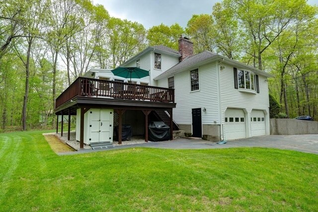 back of property with a deck, driveway, a garage, a lawn, and a chimney