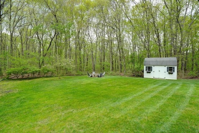 view of green lawn with an outbuilding, a storage shed, and a forest view