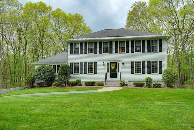 colonial inspired home with a front lawn, entry steps, and a shingled roof