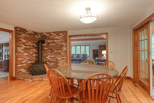 dining area with light wood-style flooring, a textured ceiling, a wood stove, and baseboards