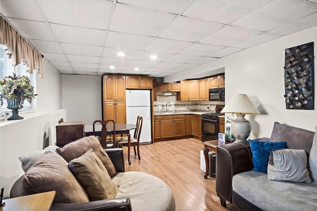 living room featuring a drop ceiling, sink, and light wood-type flooring