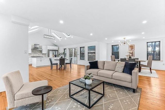 living area featuring lofted ceiling, a healthy amount of sunlight, light wood-type flooring, and a notable chandelier