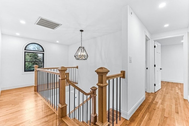 hall with light wood finished floors, visible vents, an inviting chandelier, and an upstairs landing