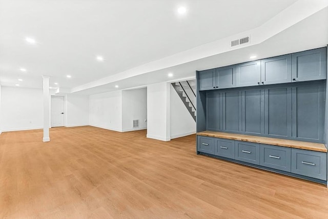 finished below grade area with stairs, visible vents, and light wood-style floors