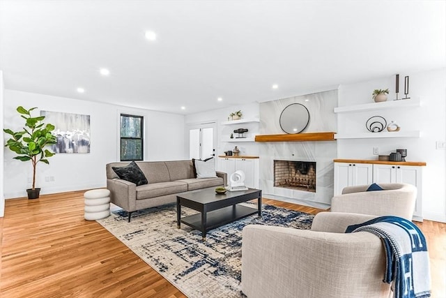 living area featuring baseboards, light wood finished floors, a high end fireplace, and recessed lighting