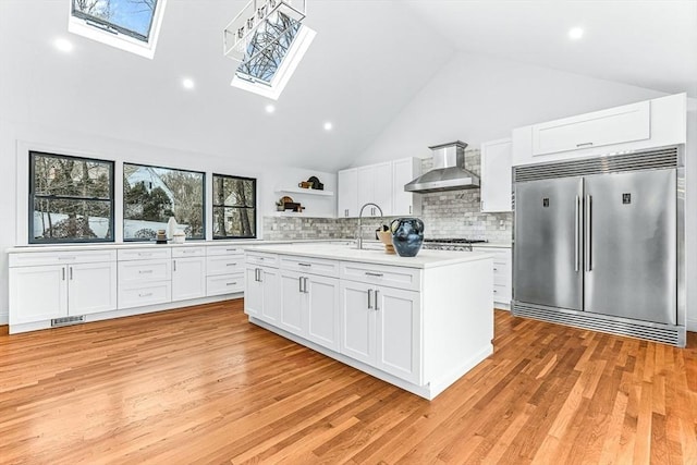 kitchen featuring a skylight, open shelves, light countertops, appliances with stainless steel finishes, and wall chimney exhaust hood