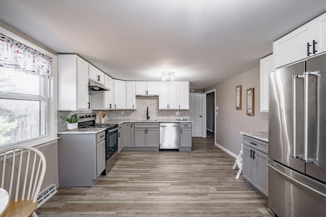 kitchen featuring light wood-type flooring, stainless steel appliances, light stone counters, and gray cabinets