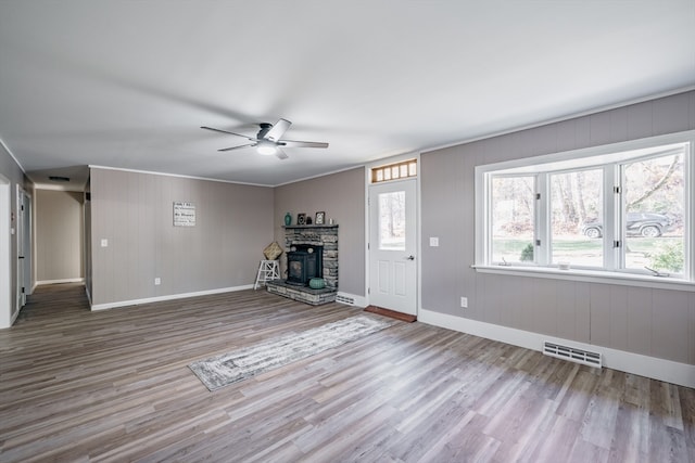 unfurnished living room featuring ornamental molding, ceiling fan, hardwood / wood-style flooring, a wood stove, and wood walls