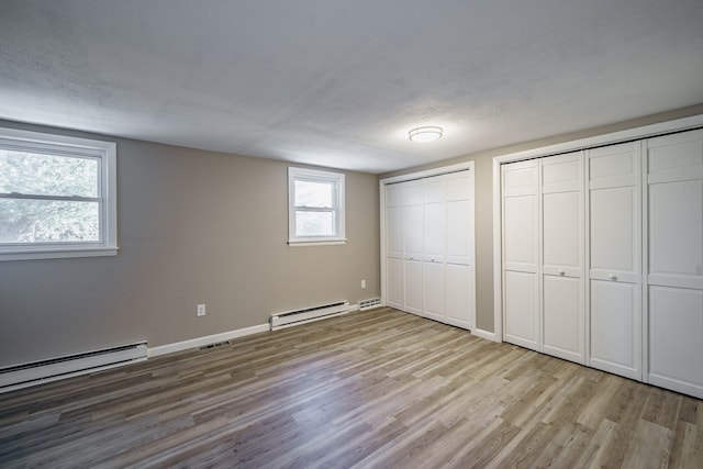 unfurnished bedroom with a textured ceiling, a baseboard radiator, two closets, and light hardwood / wood-style floors