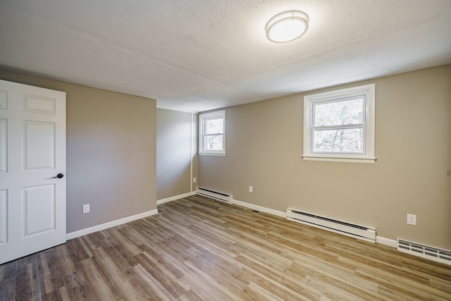 unfurnished room featuring baseboard heating, light hardwood / wood-style flooring, and a textured ceiling