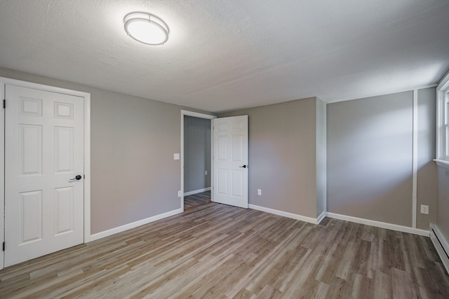 interior space with a closet, light hardwood / wood-style floors, a textured ceiling, and a baseboard heating unit