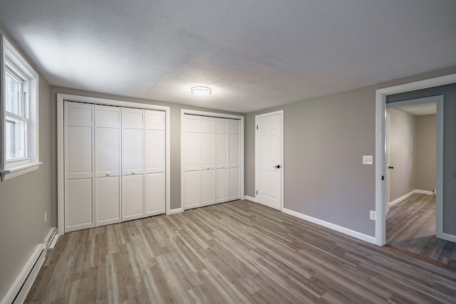 unfurnished bedroom with two closets, a baseboard radiator, light wood-type flooring, and a textured ceiling