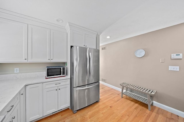 kitchen featuring appliances with stainless steel finishes, light stone countertops, light wood-type flooring, and white cabinets