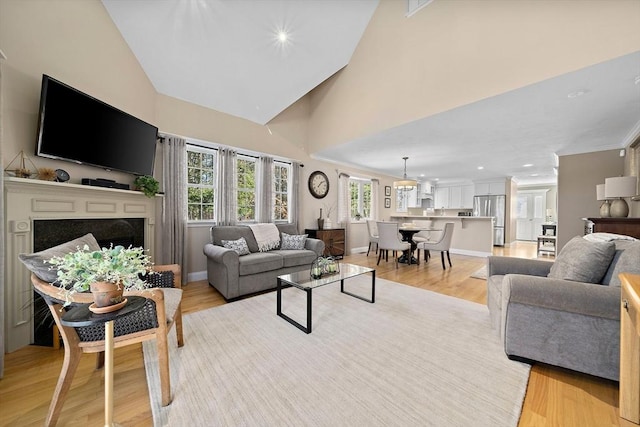 living room with a premium fireplace, high vaulted ceiling, and light wood-type flooring