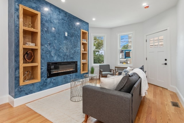 living room with built in features, light hardwood / wood-style floors, and a premium fireplace