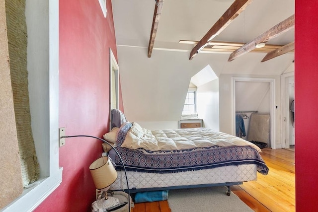 bedroom with vaulted ceiling with beams and wood finished floors