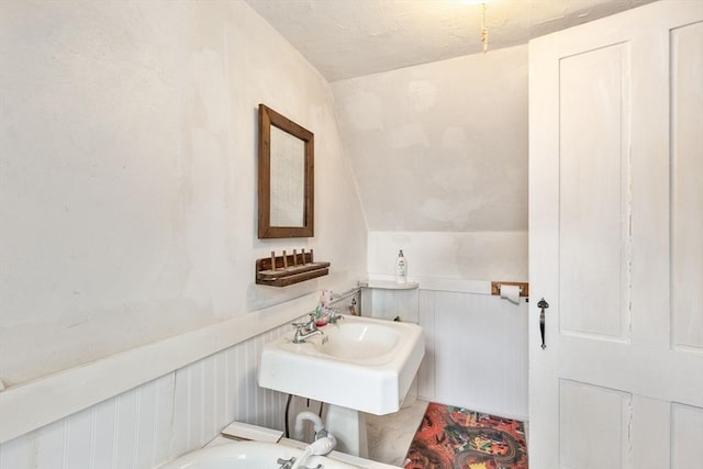 bathroom with lofted ceiling, a sink, and wainscoting