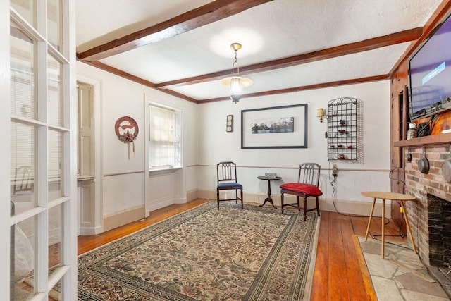 living area with a brick fireplace, baseboards, wood-type flooring, and beam ceiling