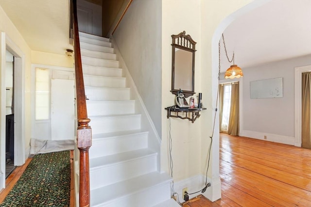 stairway with hardwood / wood-style flooring, baseboards, and arched walkways