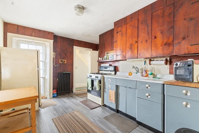 kitchen with a toaster, light countertops, light wood-style flooring, wood walls, and white appliances