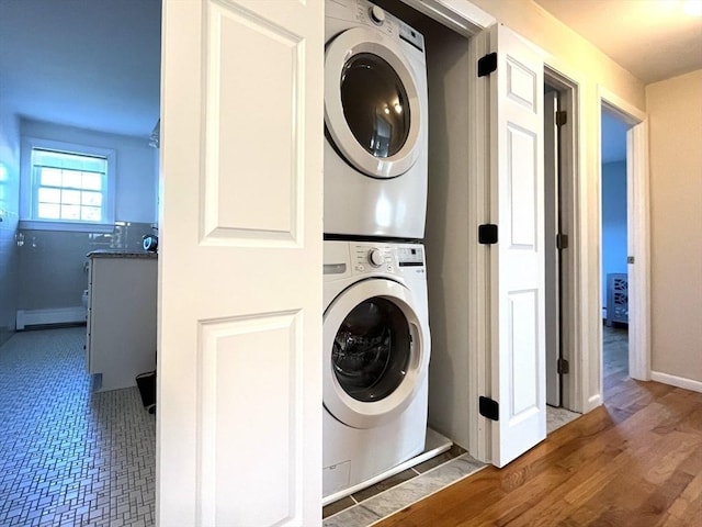 washroom with wood-type flooring, stacked washer and clothes dryer, and a baseboard heating unit