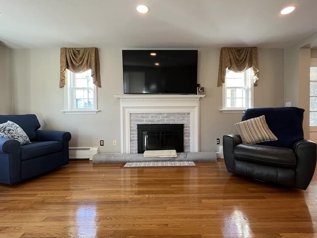 living room with a brick fireplace, hardwood / wood-style floors, and baseboard heating