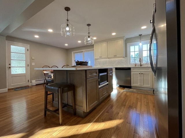 kitchen with hanging light fixtures, backsplash, stainless steel appliances, wood-type flooring, and a kitchen island