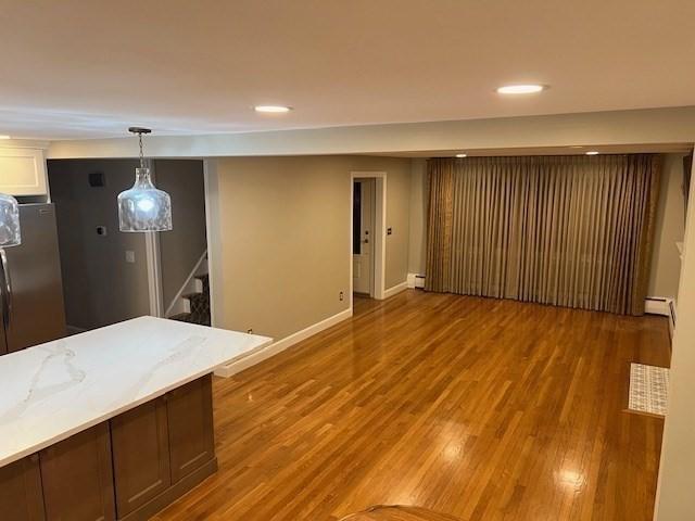 interior space with hardwood / wood-style floors, a baseboard heating unit, pendant lighting, and stainless steel refrigerator