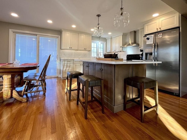 kitchen featuring white cabinetry, decorative light fixtures, stainless steel fridge with ice dispenser, decorative backsplash, and wall chimney range hood