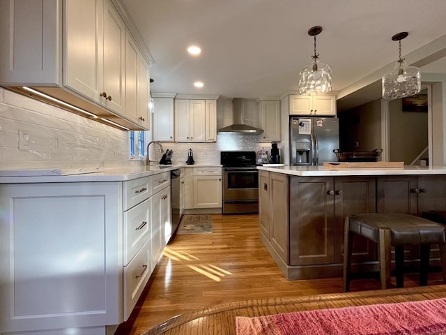 kitchen with white cabinetry, hanging light fixtures, a kitchen island, stainless steel appliances, and wall chimney range hood