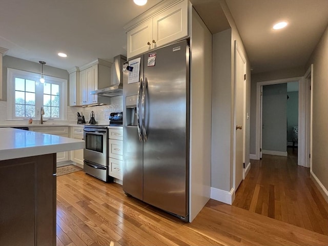 kitchen with white cabinetry, tasteful backsplash, decorative light fixtures, stainless steel appliances, and wall chimney range hood