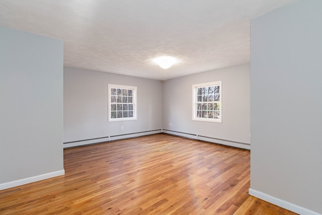 empty room with a textured ceiling, light wood-type flooring, and baseboard heating