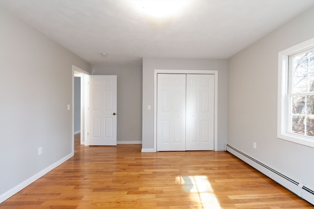 unfurnished bedroom with a closet, light hardwood / wood-style flooring, and a baseboard radiator