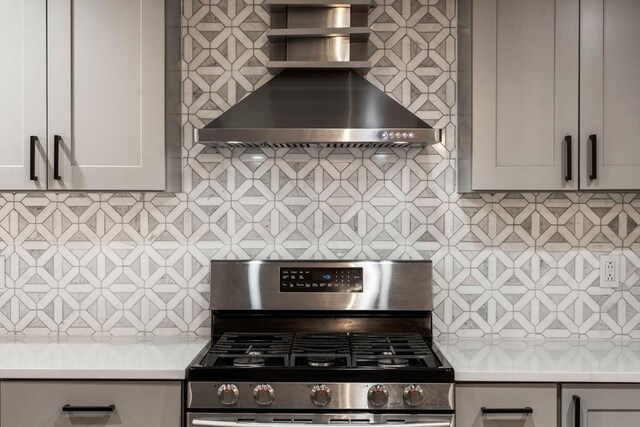 kitchen featuring gas range, wall chimney range hood, backsplash, light countertops, and gray cabinets