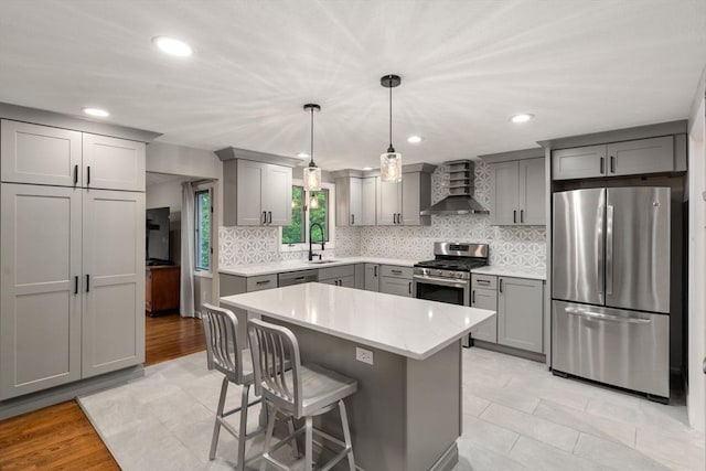 kitchen with stainless steel appliances, wall chimney exhaust hood, gray cabinetry, a sink, and tasteful backsplash