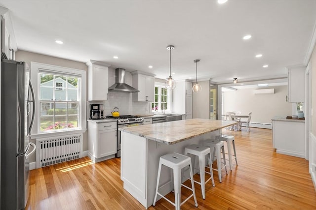 38 Fairmount Rd, Reading, MA 01867 - kitchen with wall chimney exhaust hood, radiator heating unit, stainless steel appliances, a baseboard radiator, and a kitchen island