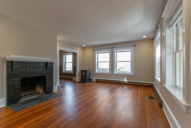 unfurnished living room featuring wood-type flooring, a fireplace, a baseboard radiator, baseboards, and a wood stove