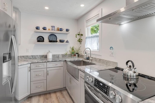 853 Sandwich, Falmouth, MA 02536 - kitchen featuring stainless steel appliances, wall chimney exhaust hood, light wood-style flooring, a sink, and light stone counters